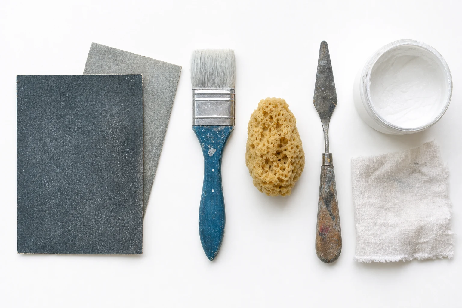 Overzicht van materialen voor doekvoorbereiding: gesso, schuurpapier, kwast, roller en schilderstape