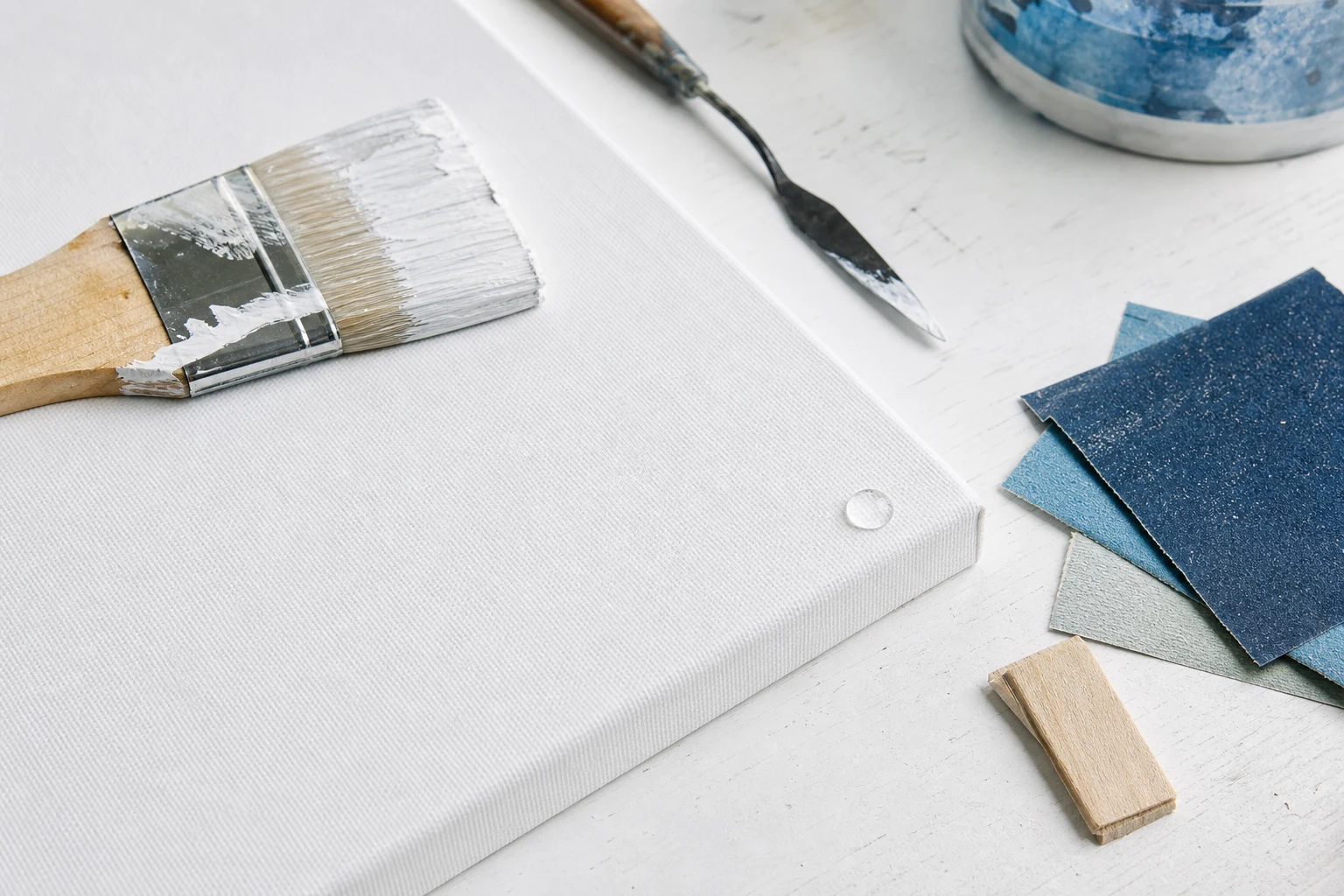 Witte doekwerkplaats met gesso, breed schildersgereedschap en een opgespannen doek op een schildersframe