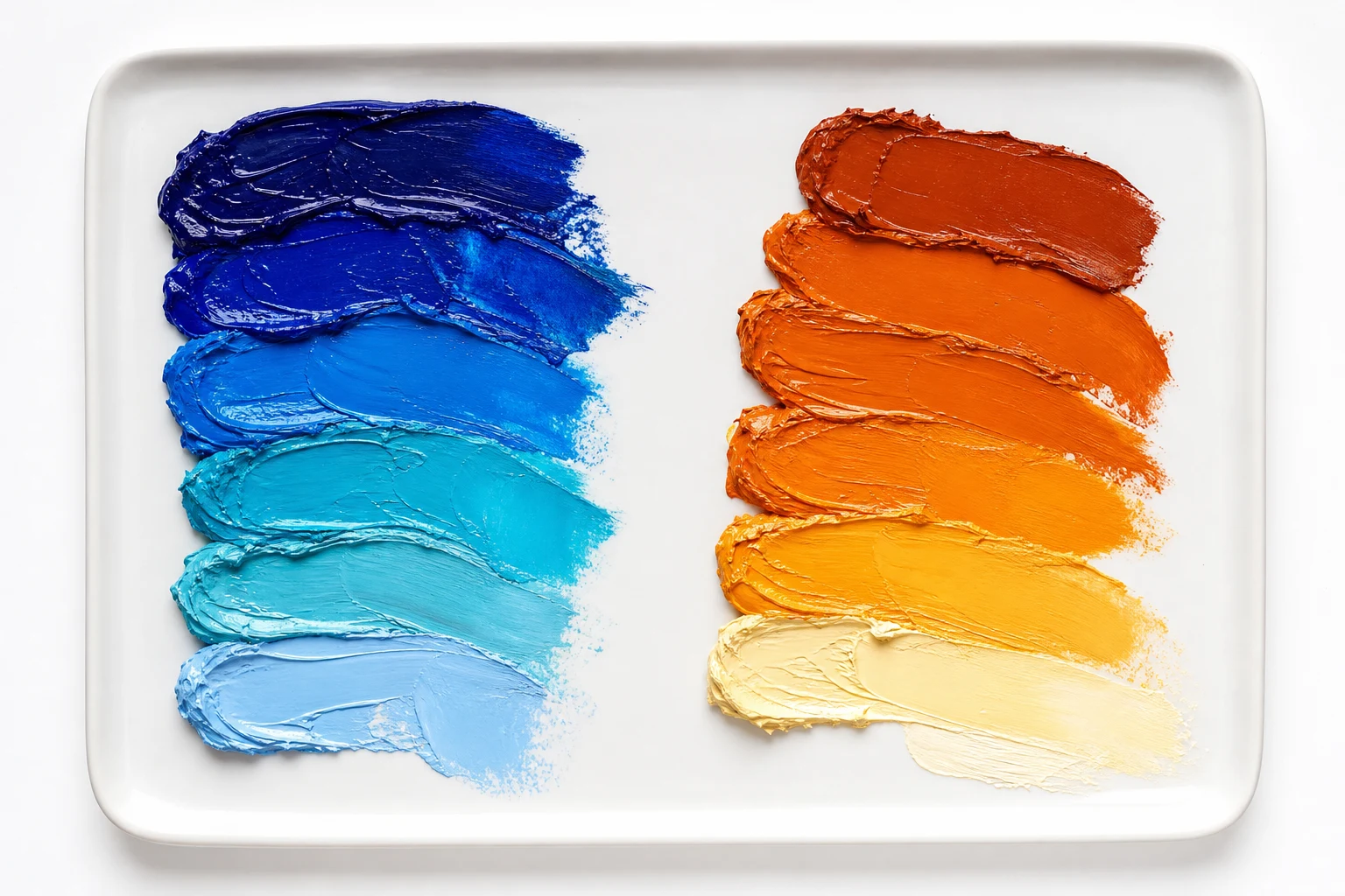 Paletstudie met blauwe en oranje verffamilies naast elkaar uitgesmeerd op een witte tegel, van diep blauw naar koel lichtblauw en van donker oranje naar bijna wit