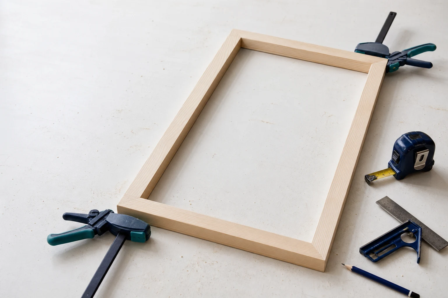 Houten frame in droogpassing op een witte werkbank met winkelhaak, meetlint en lijmklemmen