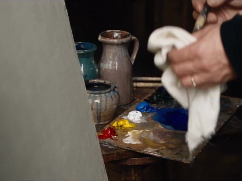 Still uit de AI-film: houten palet met klodders rood, geel, wit en blauw naast aardewerken kannen