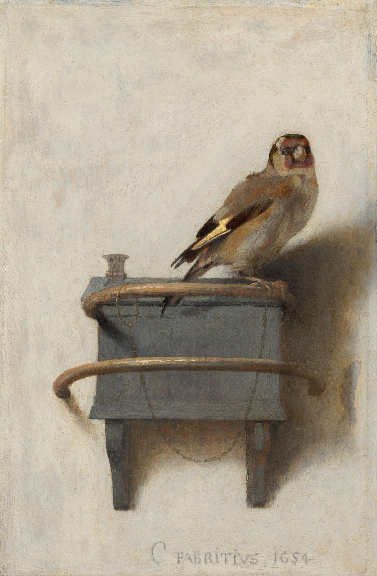 Het puttertje van Carel Fabritius: een klein distelvinkje op een voederbakje aan een lichte muur, vastgemaakt aan een kettinkje